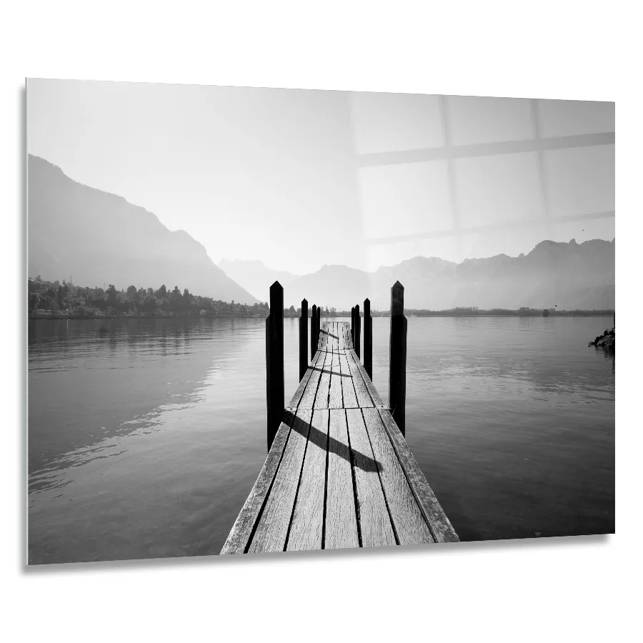 182074922_90x60cm A 90x60cm landscape glass print of a tranquil black and white wooden pier leading to a lake, with mountains silhouetted in the background.