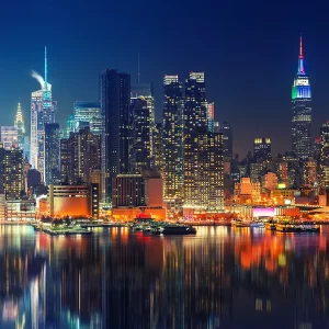 A closeup glass print, picturing the skyline of Manhattan at night, with glowing lights reflected on the water.
