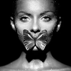 A glass print in black and white of a close up of a beautiful woman covered in sparkles with a butterfly covering her mouth.