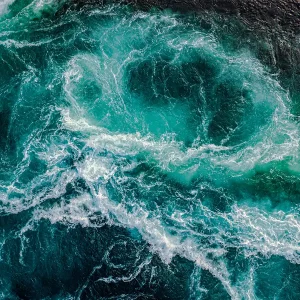 glass wall art captures an aerial view of turquoise ocean waves