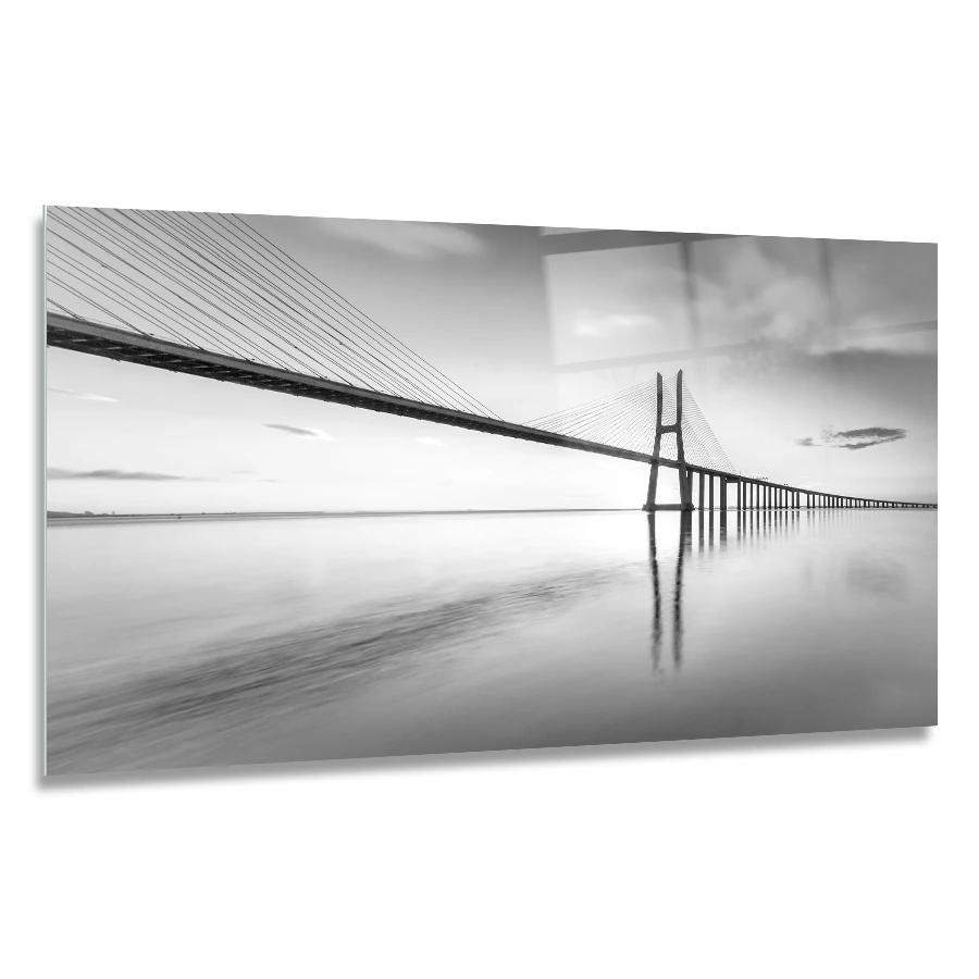 90075971-bridge-vasco-da-gama-120x60 landscape glass print of Black and white photo of a long, sleek cable-stayed bridge reflecting in calm water under a cloudy sky.